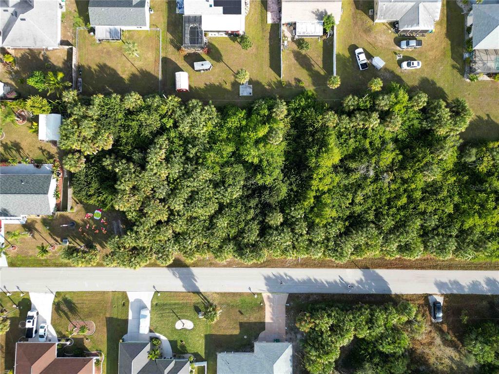 An aerial view shows a vacant, heavily wooded rectangular lot situated between residential properties — 18699 ASHCROFT CIRCLE, PORT CHARLOTTE, FL