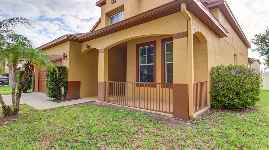 A tan house exterior features a covered front porch with a metal railing and landscaping — 13659 ARTESA BELL DRIVE, RIVERVIEW, FL