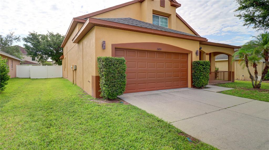 A tan two-story house features a brown garage door, a concrete driveway, and manicured hedges — 13659 ARTESA BELL DRIVE, RIVERVIEW, FL