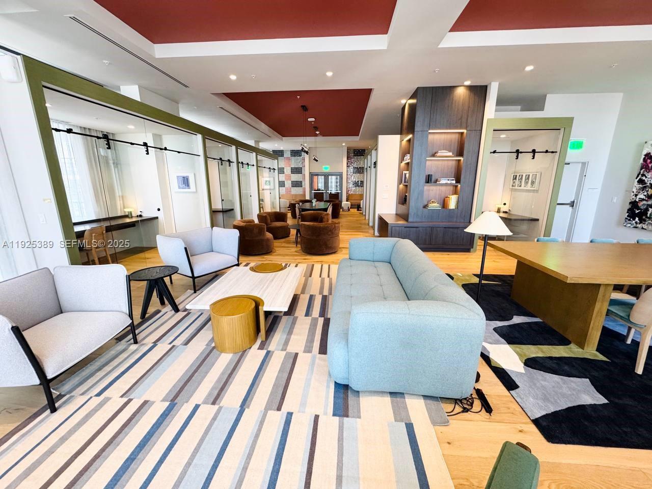 A modern lounge area features a blue sofa, armchairs, patterned rugs, and private glass-enclosed workspaces — 11 NE 6th # 2813, Miami FL 33132, MIAMI, FL