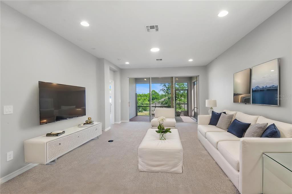 A living room features a wall-mounted television, white furniture, carpeted flooring, and sliding glass doors — 2017 BOSS HEWETT STREET, OAKLAND, FL