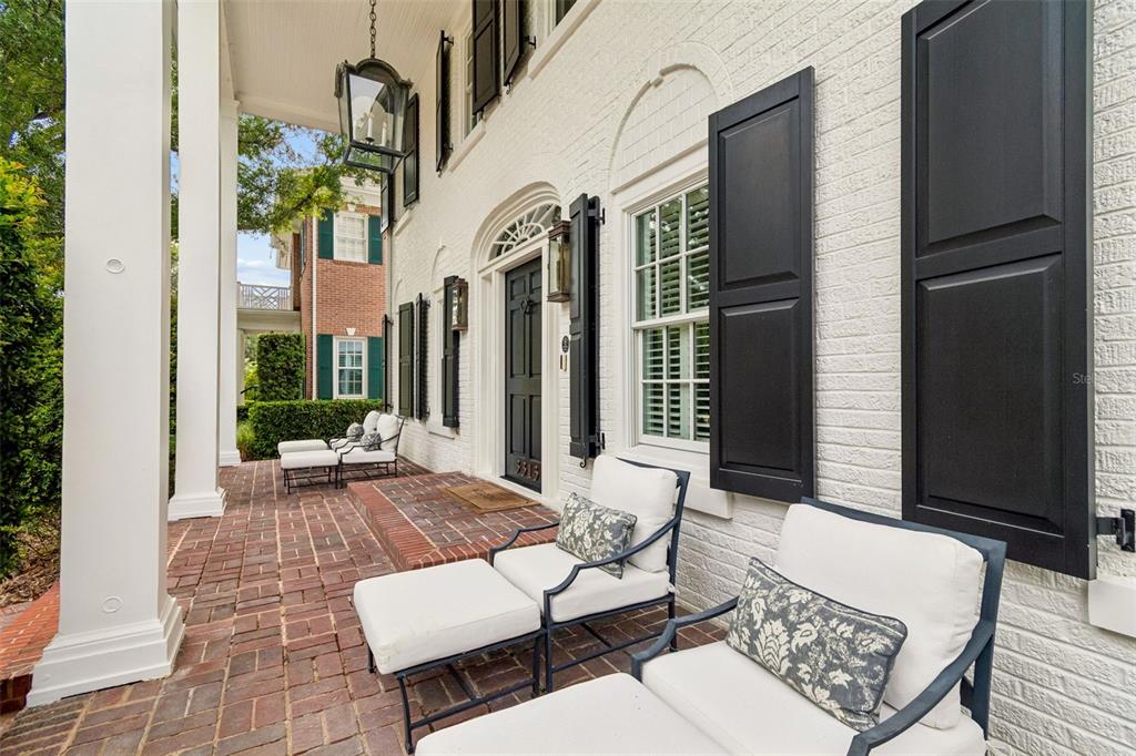 A white brick porch features black shutters, a dark front door, and outdoor lounge chairs — 3313 W MULLEN AVENUE, TAMPA, FL