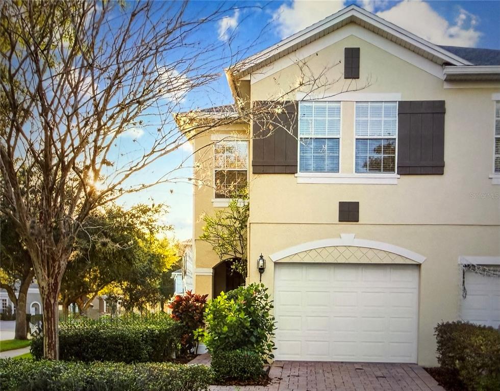 A side view of a two-story tan stucco townhouse with multiple windows and landscaping — 3115 CAPRI ISLE WAY, ORLANDO, FL