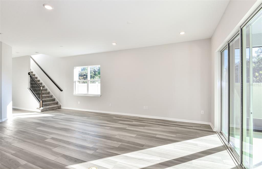 A kitchen with white cabinets, a central island, and light wood flooring opens to a living area — 1361 ALLAGASH DRIVE, ZEPHYRHILLS, FL