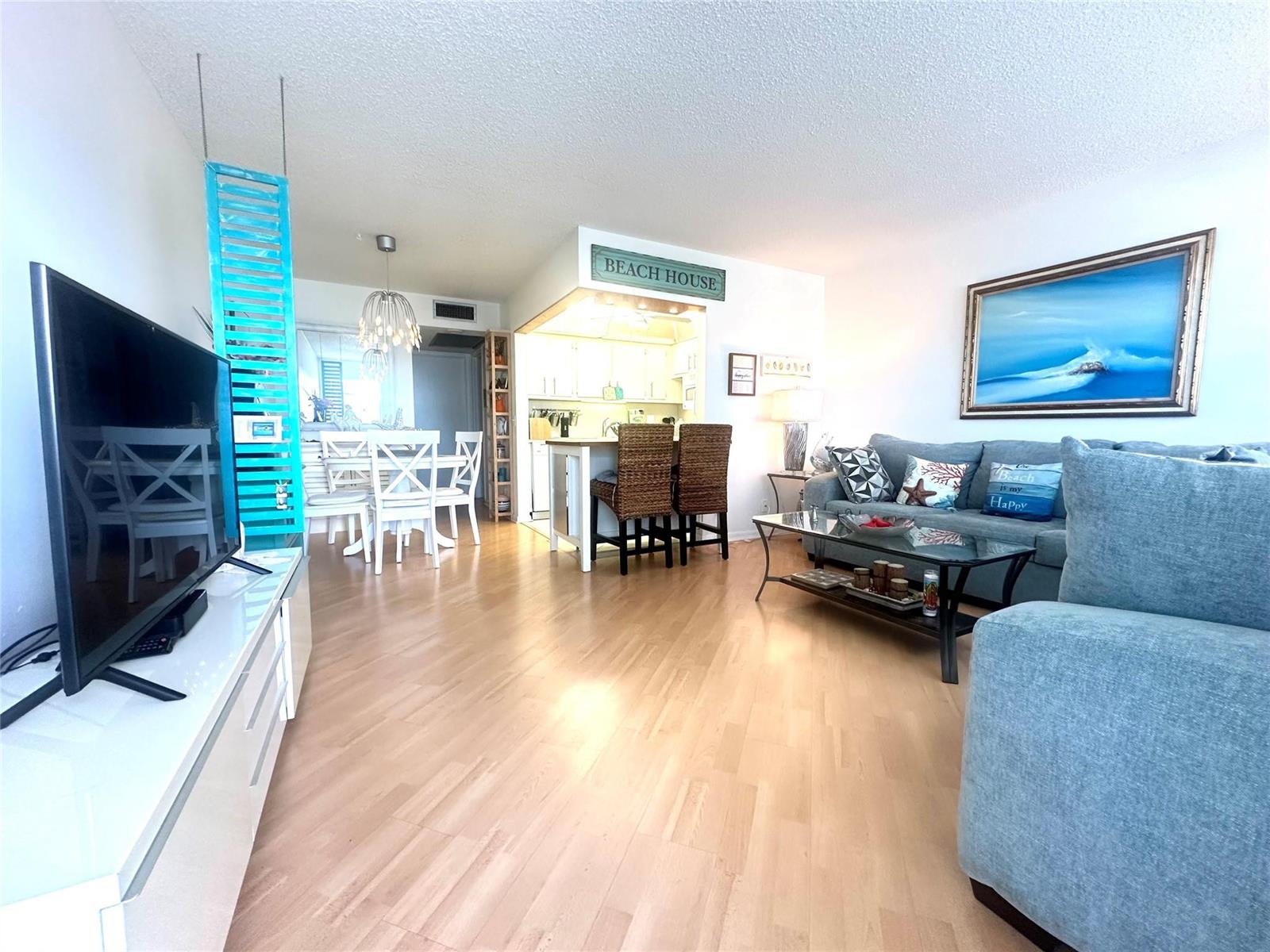An open-concept living and dining area features light wood flooring and beach-themed decor — 2004 Harwood C # 2004, Deerfield Beach FL 33442, DEERFIELD BEACH, FL
