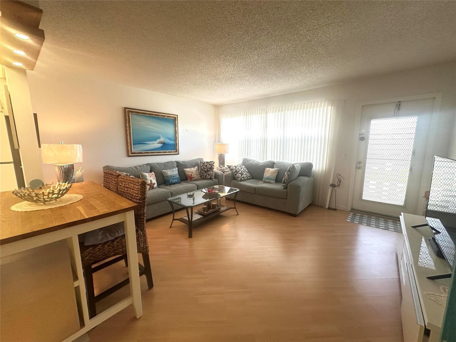 A living room features light wood flooring, two gray sofas, and a glass coffee table — 2004 Harwood C # 2004, Deerfield Beach FL 33442, DEERFIELD BEACH, FL