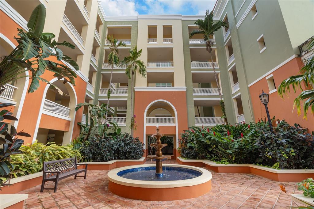 A courtyard with a tiered fountain, a wooden bench, and tropical plants between apartment buildings — 500 OCEAN DRIVE UNIT 553, HUMACAO, PR