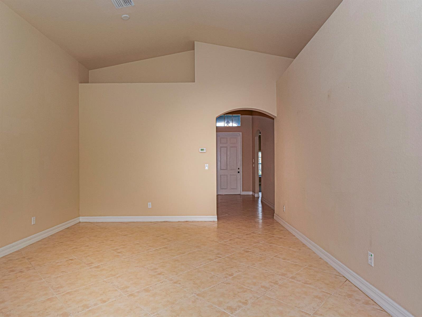 An empty room with beige walls, vaulted ceilings, and light-colored tile flooring — 5561 57th Way, Vero Beach FL 32967, VERO BEACH, FL