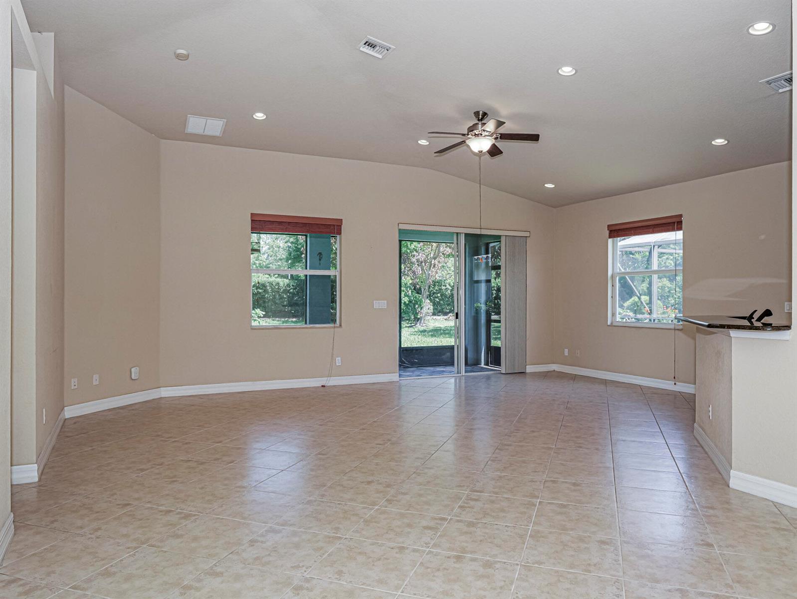 A spacious, empty living room features beige tile flooring, recessed lighting, and a ceiling fan — 5561 57th Way, Vero Beach FL 32967, VERO BEACH, FL