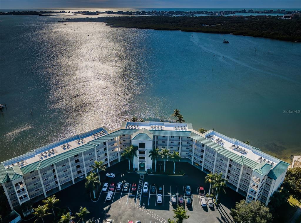 An aerial view shows a multi-story waterfront apartment building with a parking lot and palm trees — 8800 BAY PINES BOULEVARD UNIT 303, ST PETERSBURG, FL