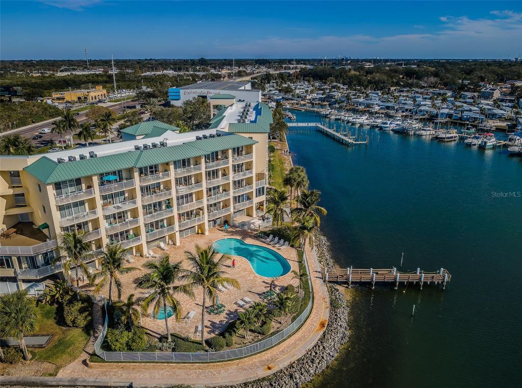 An aerial view shows a multi-story waterfront building with a pool and a boat dock — 8800 BAY PINES BOULEVARD UNIT 303, ST PETERSBURG, FL