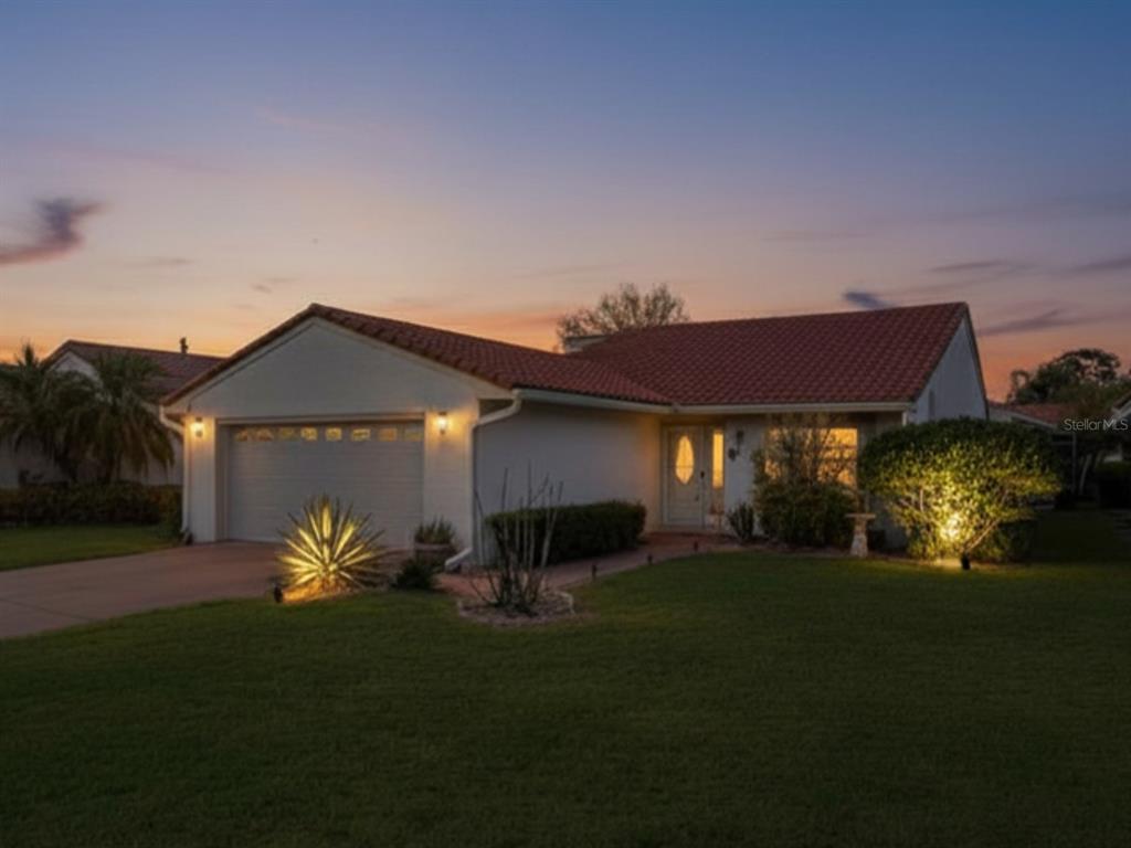 A single-story house with a tile roof, garage, and illuminated landscaping at sunset — 688 AUGUSTA ROAD, WINTER HAVEN, FL
