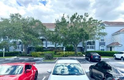 A multi-story apartment building is viewed from a parking lot with several parked cars — 14036 FAIRWAY ISLAND DRIVE UNIT 1535, ORLANDO, FL
