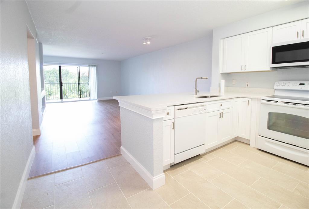 A kitchen with white cabinets and appliances overlooks a living area with wood-look flooring — 14036 FAIRWAY ISLAND DRIVE UNIT 1535, ORLANDO, FL