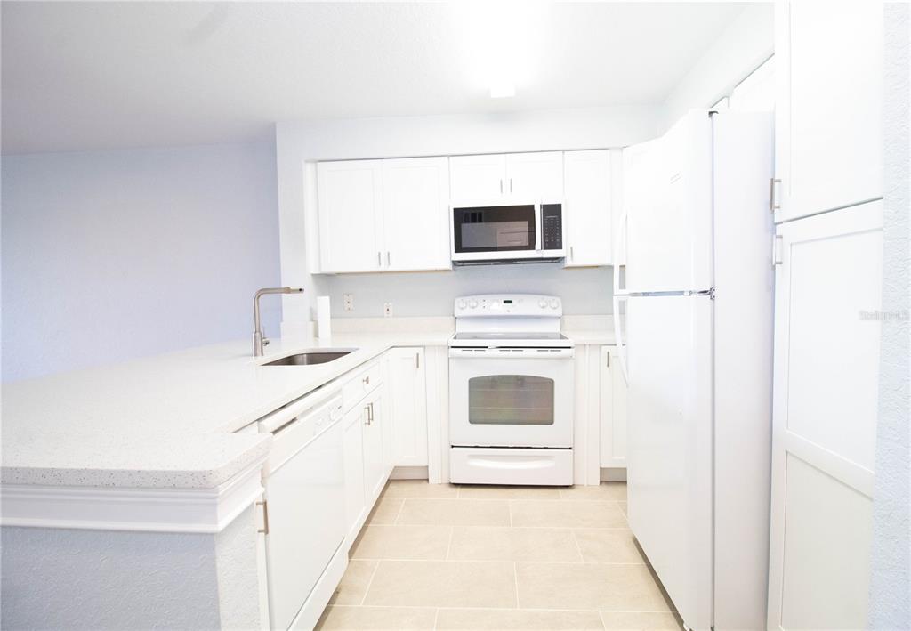 A kitchen features white cabinets, white appliances, a light-colored countertop, and tile flooring — 14036 FAIRWAY ISLAND DRIVE UNIT 1535, ORLANDO, FL