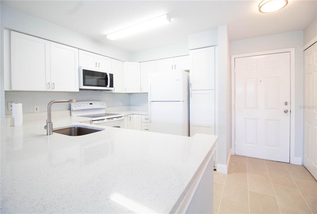 A kitchen features white cabinets, quartz countertops, a stainless steel sink, and white appliances — 14036 FAIRWAY ISLAND DRIVE UNIT 1535, ORLANDO, FL