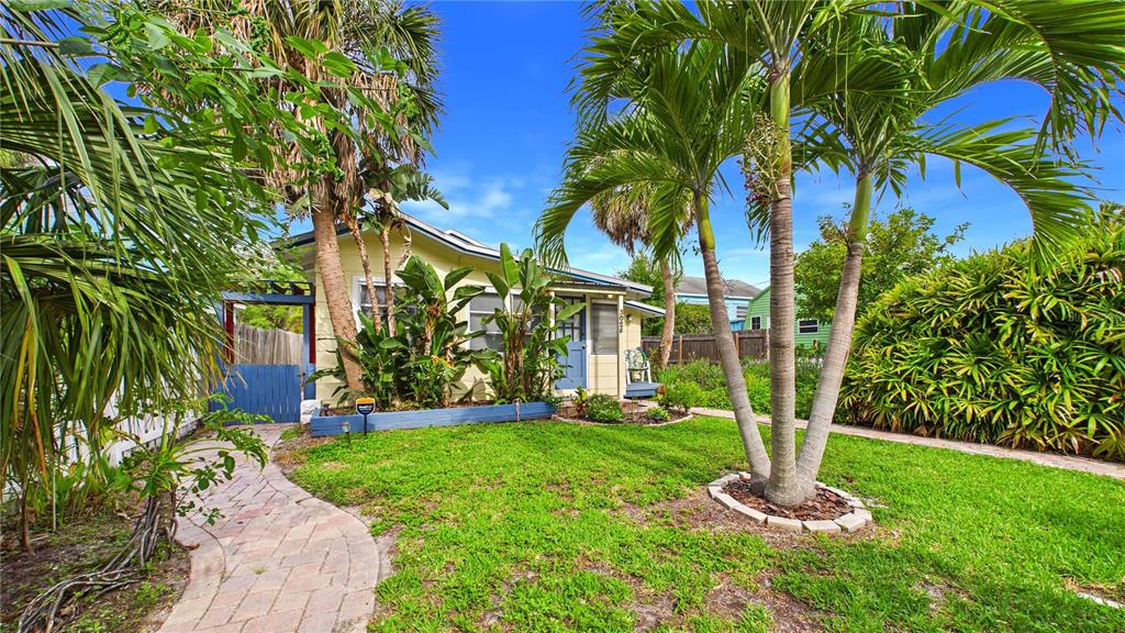 A yellow house with a blue door and gate sits behind a palm-filled front yard — 3025 56TH STREET S, GULFPORT, FL