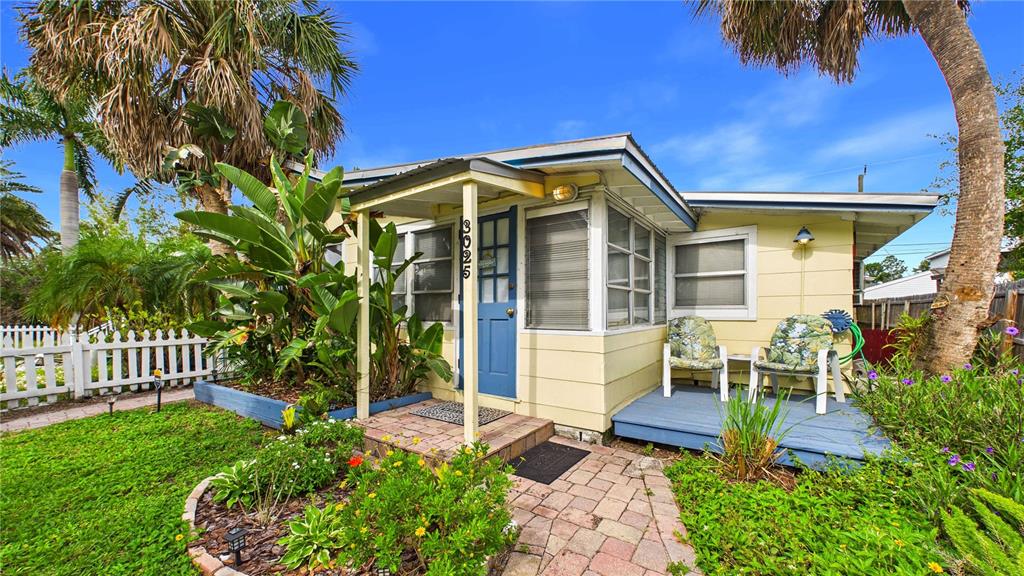 A yellow cottage features a blue front door, a small porch, and a brick walkway — 3025 56TH STREET S, GULFPORT, FL