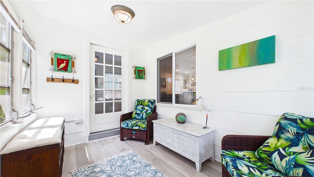 A sunroom features white shiplap walls, light wood-look flooring, and two wicker chairs with cushions — 3025 56TH STREET S, GULFPORT, FL