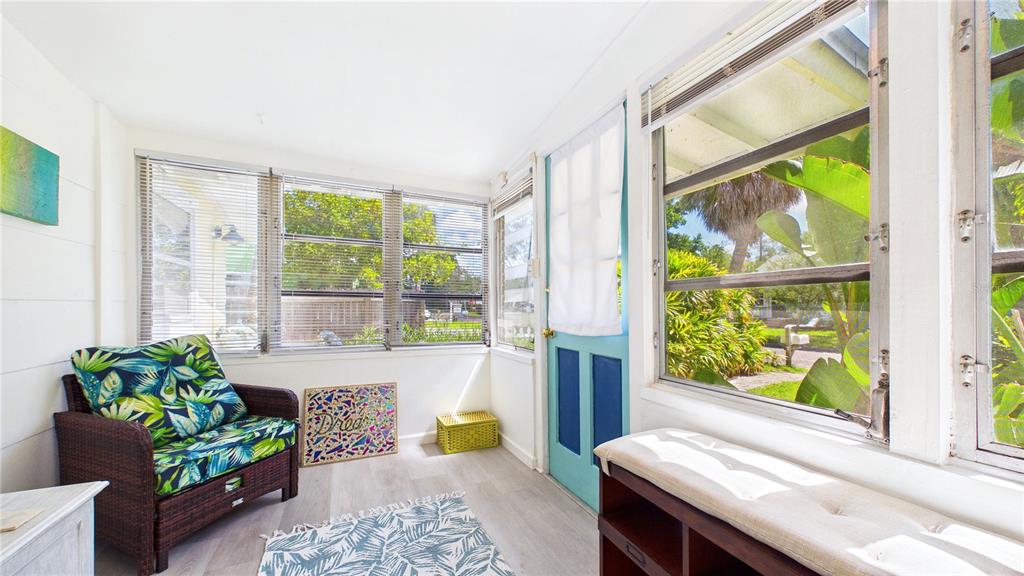 A sunroom with white walls, light wood flooring, a wicker chair, and large windows — 3025 56TH STREET S, GULFPORT, FL
