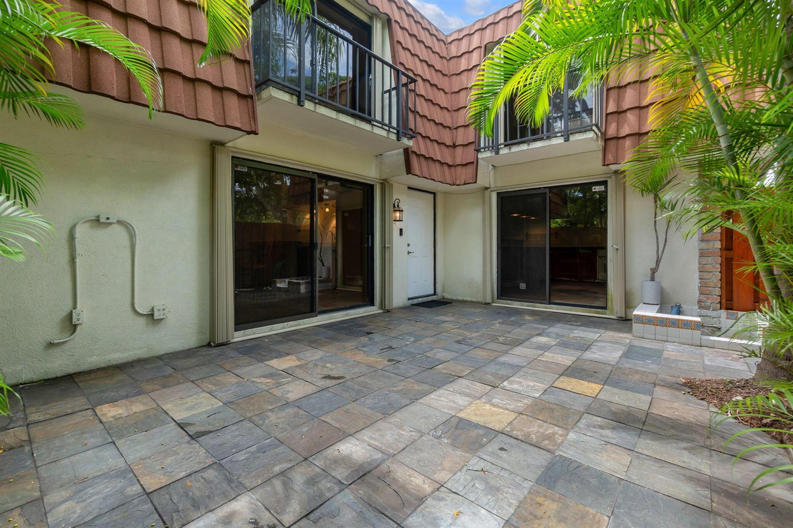 A paved patio area sits between two sliding glass doors and a white entry door — 1840 San Juan Drive # c, Delray Beach FL 33445, DELRAY BEACH, FL