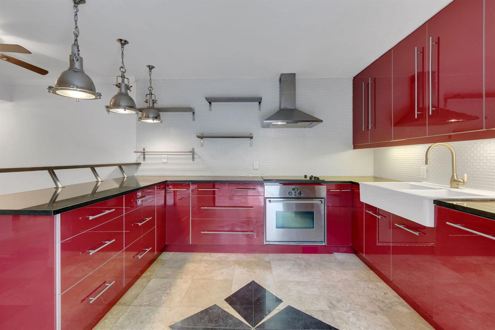 A kitchen features red high-gloss cabinets, stainless steel appliances, open shelving, and a white farmhouse sink — 1840 San Juan Drive # c, Delray Beach FL 33445, DELRAY BEACH, FL