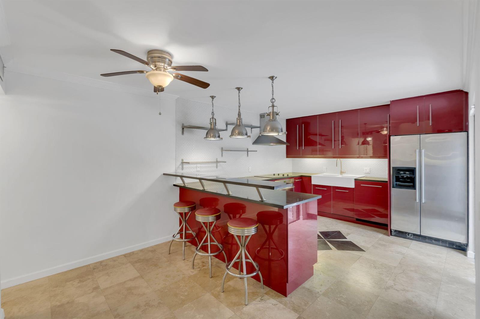 A kitchen features glossy red cabinets, a black countertop breakfast bar, and stainless steel appliances — 1840 San Juan Drive # c, Delray Beach FL 33445, DELRAY BEACH, FL