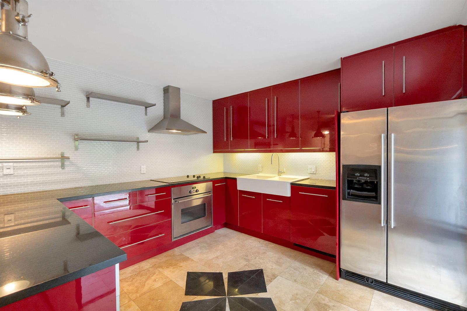 A kitchen features red high-gloss cabinets, stainless steel appliances, and a white farmhouse sink — 1840 San Juan Drive # c, Delray Beach FL 33445, DELRAY BEACH, FL