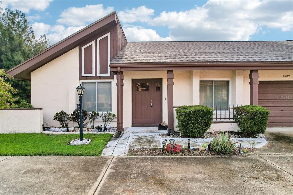 A single-story house with a brown front door, a sloped roof, and a concrete driveway — 1329 NEW BEDFORD DRIVE, SUN CITY CENTER, FL