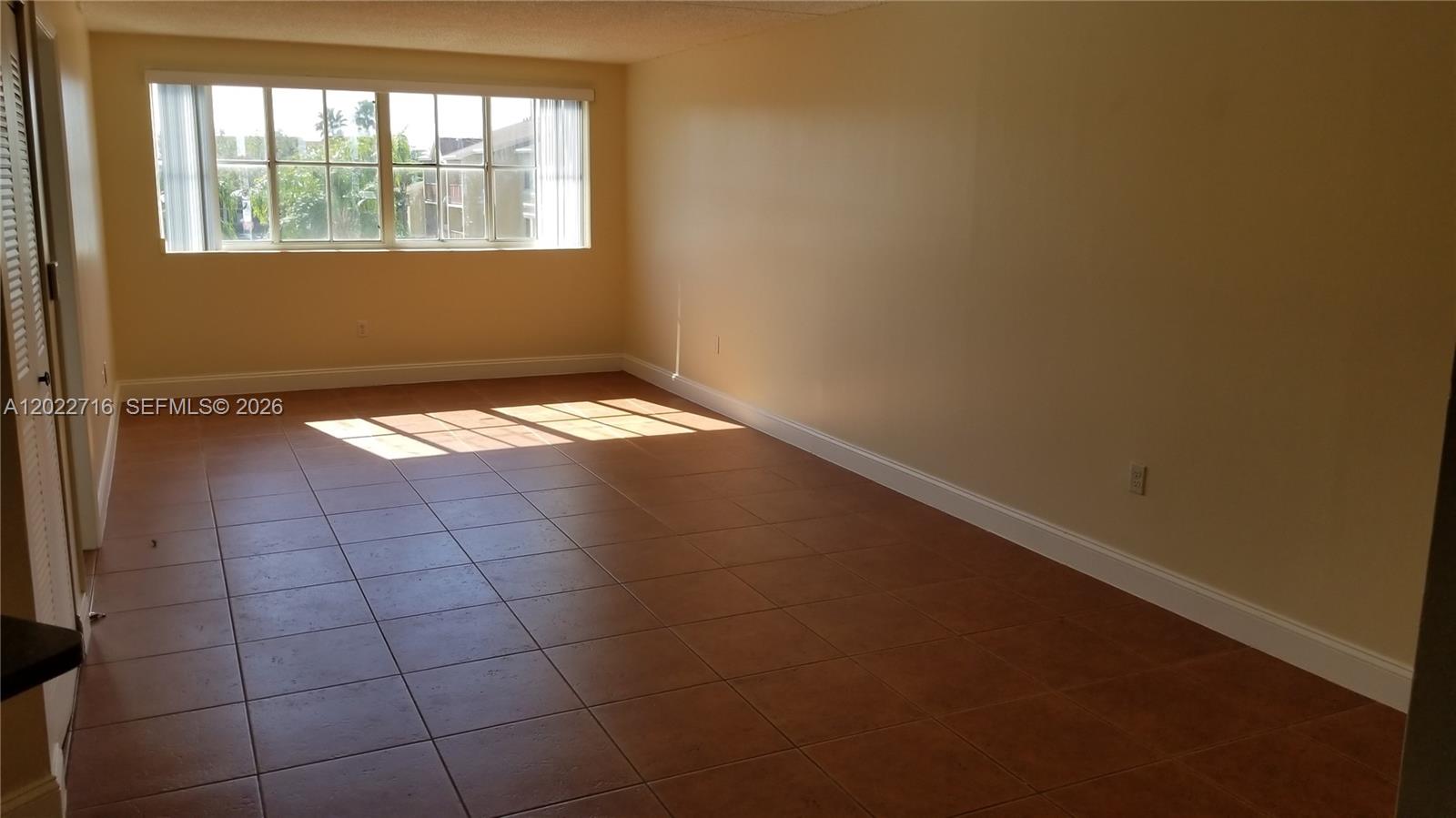 An empty room features tan walls, brown tile flooring, and a large multi-pane window — HIALEAH, FL