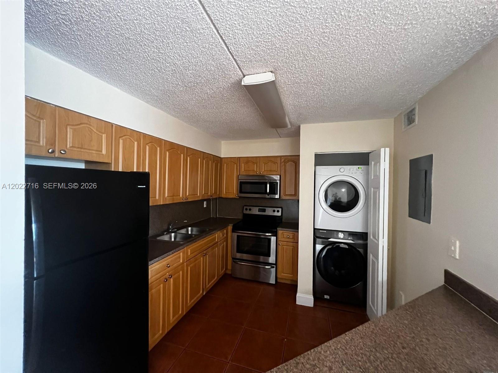 A kitchen features wood cabinets, stainless steel appliances, a black refrigerator, and a stacked washer-dryer — HIALEAH, FL