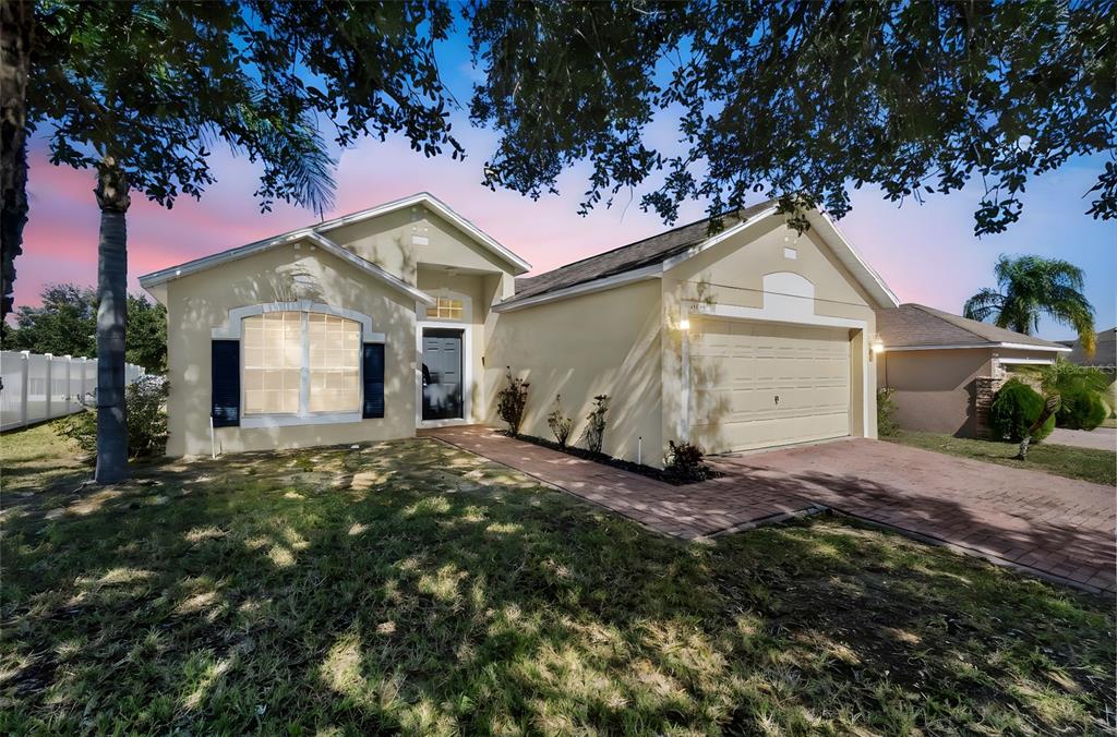 A single-story house with a beige stucco exterior, a two-car garage, and a brick driveway — 3004 PATTERSON GROVES DRIVE, HAINES CITY, FL