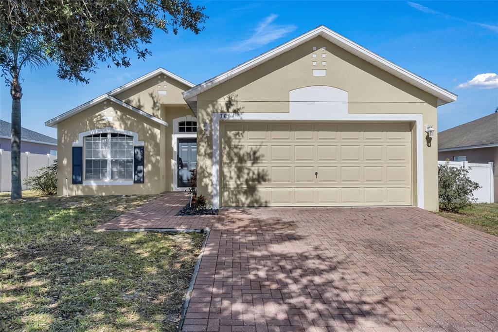 A single-story house with a tan stucco exterior, a brick driveway, and a two-car garage — 3004 PATTERSON GROVES DRIVE, HAINES CITY, FL