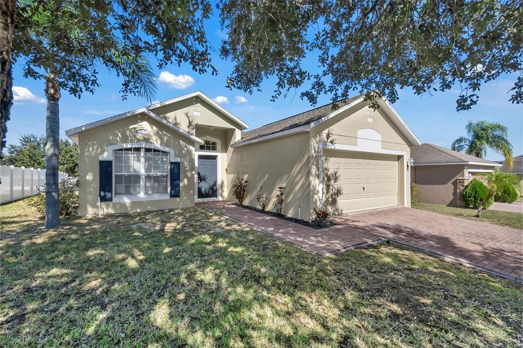 A single-story house with a beige stucco exterior, a two-car garage, and a brick walkway — 3004 PATTERSON GROVES DRIVE, HAINES CITY, FL