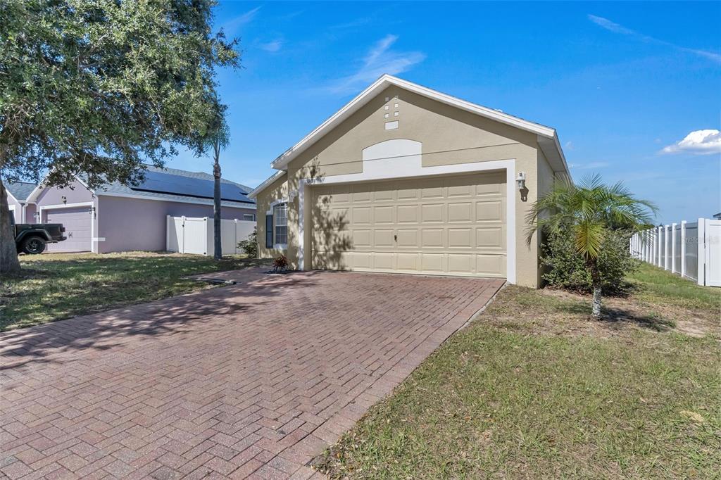 A tan single-story house features a two-car garage and a brick paver driveway — 3004 PATTERSON GROVES DRIVE, HAINES CITY, FL