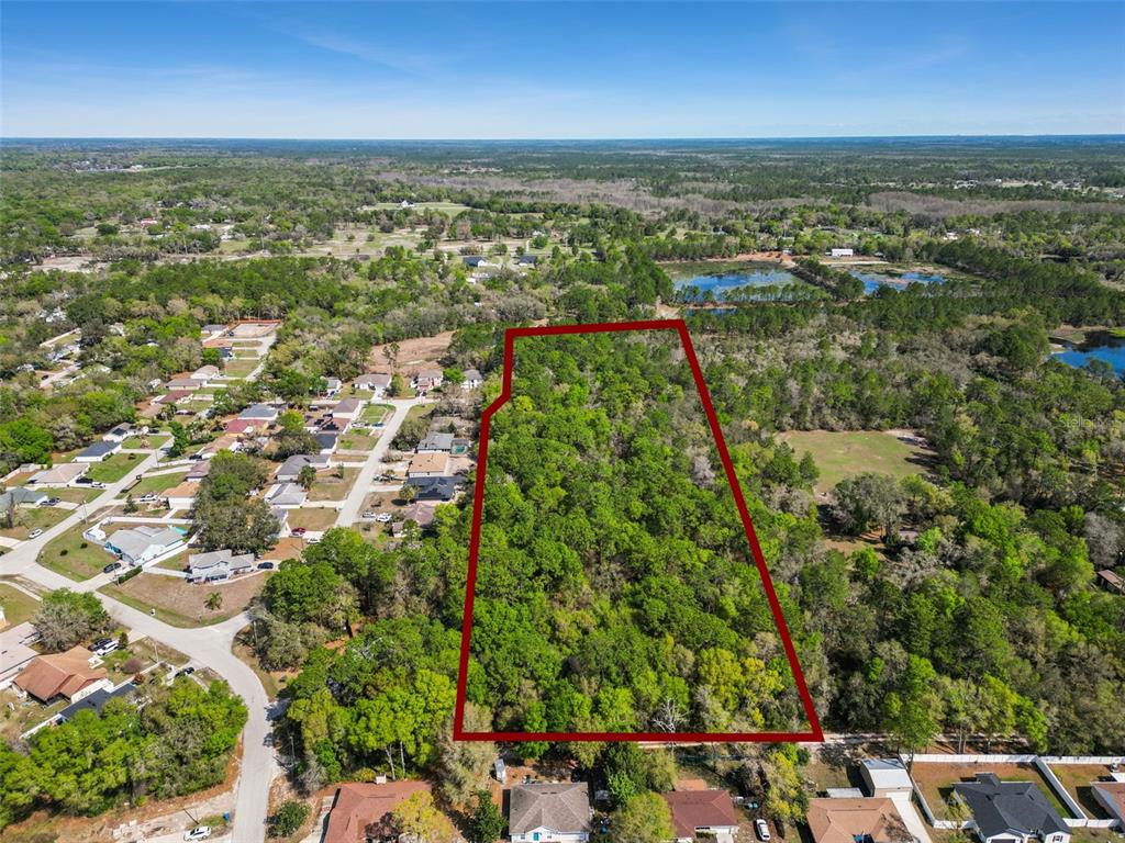 An aerial view shows a rectangular, wooded plot of land outlined in red near houses — 2130 MISSOULA TRAIL, DELTONA, FL