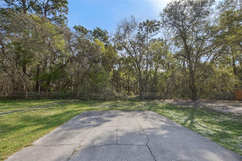 A cracked concrete driveway leads toward a wooden fence bordering a dense, wooded area — 2130 MISSOULA TRAIL, DELTONA, FL