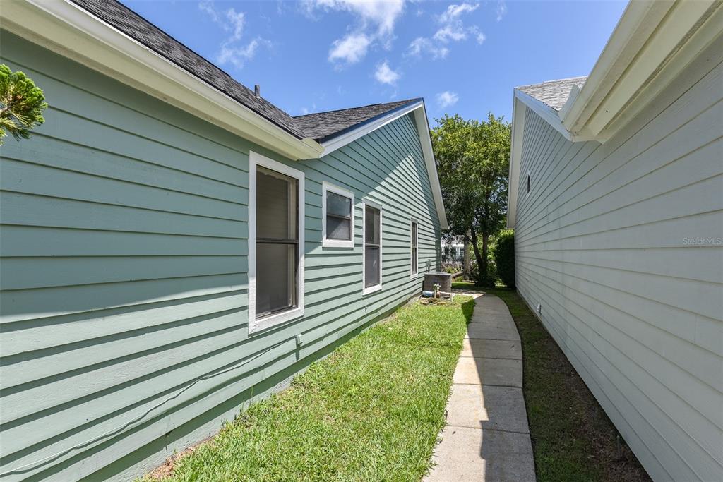 A narrow walkway separates two light green houses with horizontal siding under a blue sky — 756 PINE SHORES CIRCLE, NEW SMYRNA BEACH, FL