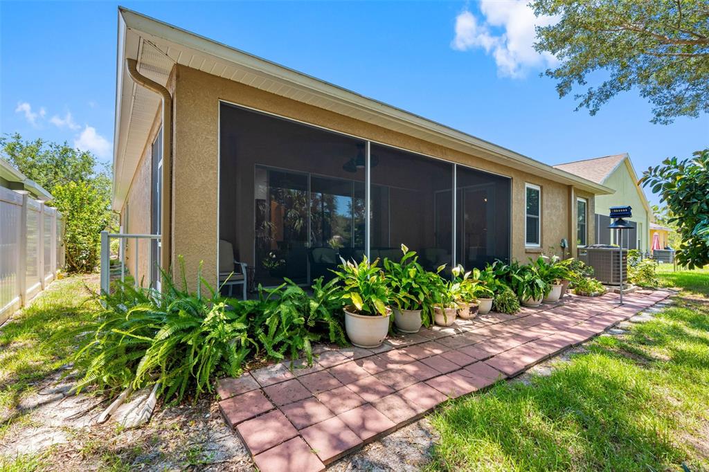 A tan house exterior features a screened-in patio with potted plants and a brick walkway — 5335 CLOVER MIST DRIVE, APOLLO BEACH, FL