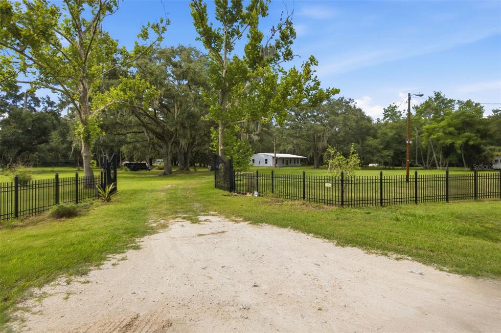 A dirt driveway leads through an open gate toward a house surrounded by large trees — 18127 CEDARHURST ROAD, ORLANDO, FL