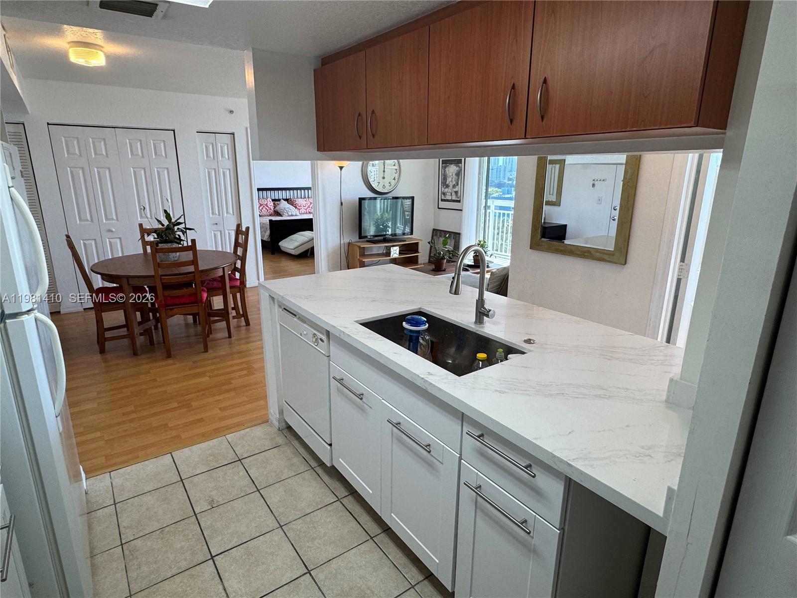 A kitchen with white cabinets and marble countertops overlooks a dining area and living room — 816 NW 11th St # 1108, Miami FL 33136, MIAMI, FL