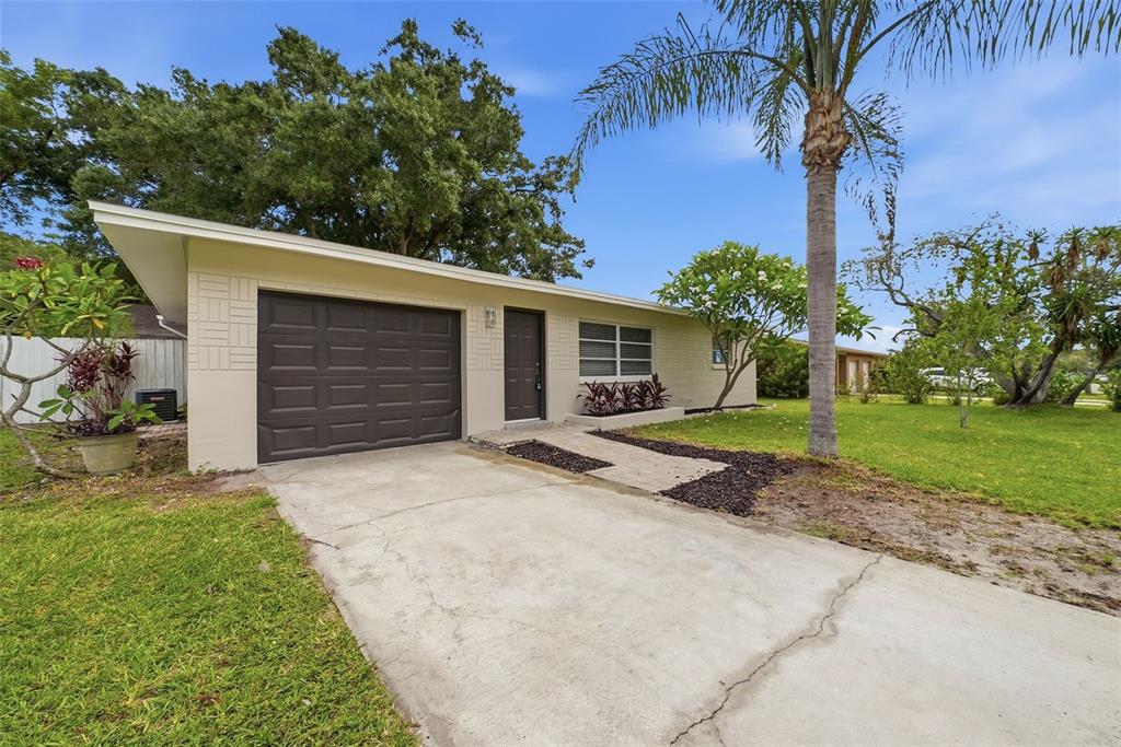 A single-story house with a beige brick exterior, a dark garage door, and a palm tree — 11325 110TH AVENUE, LARGO, FL