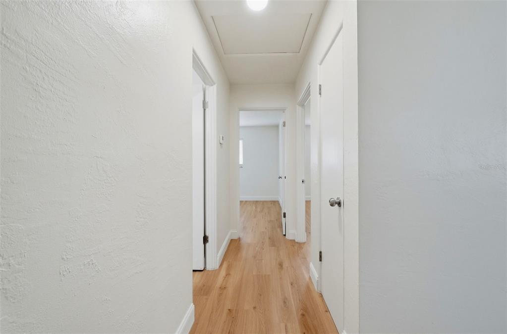 A hallway with white walls, light wood-look flooring, and several closed white doors — 11325 110TH AVENUE, LARGO, FL