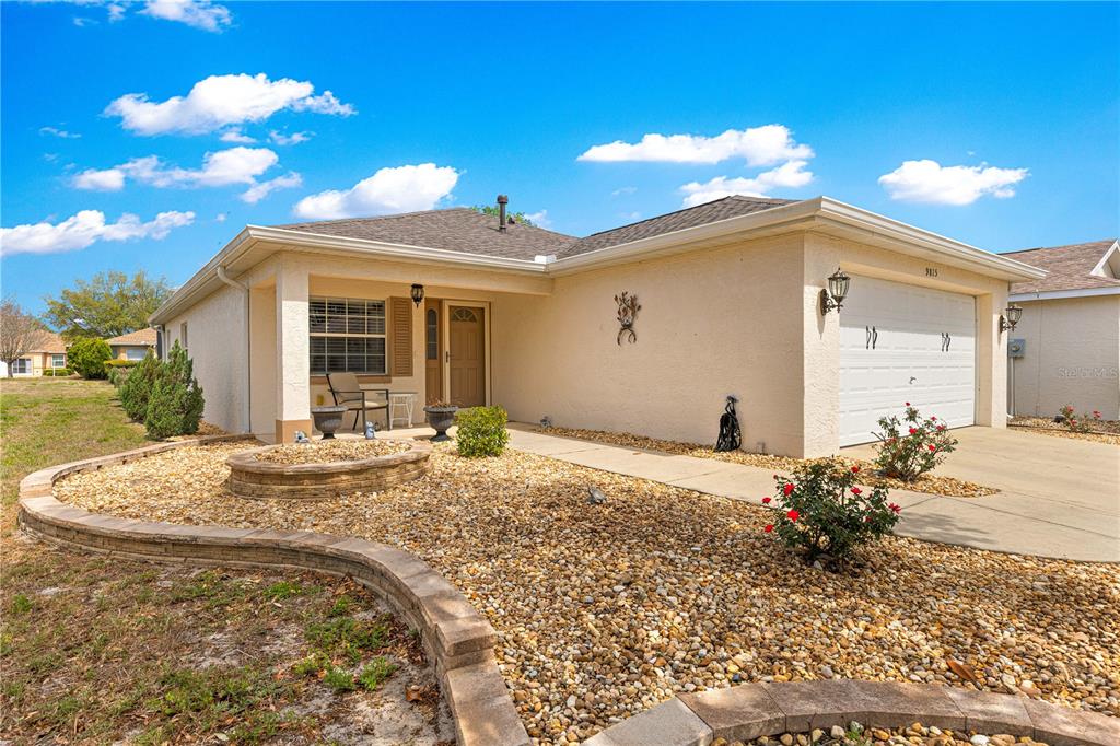 A single-story house with a beige stucco exterior, a two-car garage, and a gravel yard — 9815 SW 92ND PLACE ROAD, OCALA, FL