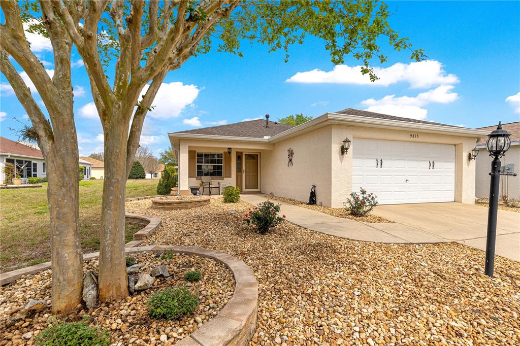 A single-story house with a beige stucco exterior, a two-car garage, and a gravel yard — 9815 SW 92ND PLACE ROAD, OCALA, FL