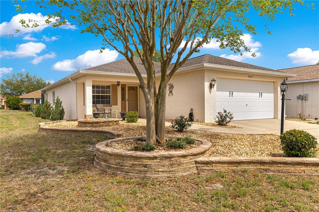 A single-story house with a beige stucco exterior, a two-car garage, and a stone-walled planter — 9815 SW 92ND PLACE ROAD, OCALA, FL