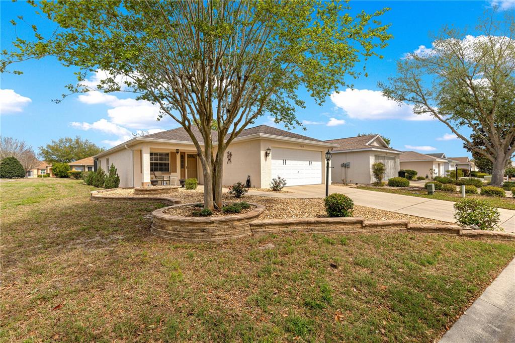 A single-story house with a beige stucco exterior, a two-car garage, and a tiered stone planter — 9815 SW 92ND PLACE ROAD, OCALA, FL