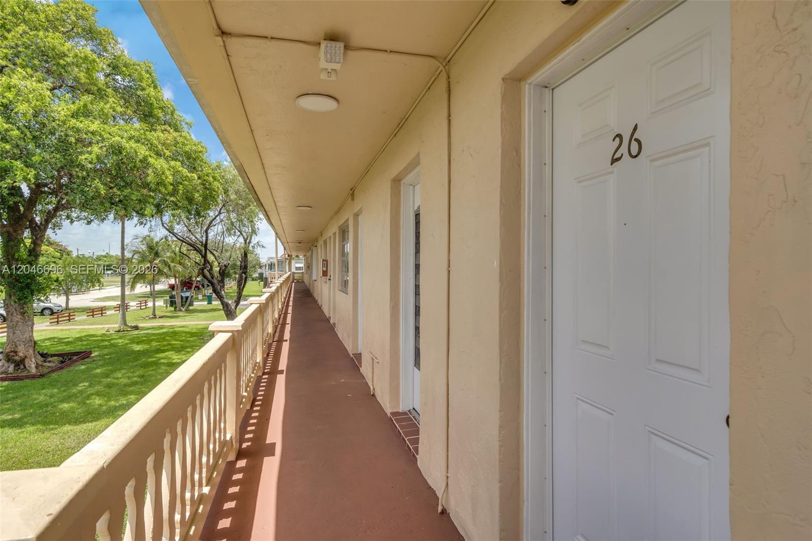 An exterior walkway with a white door numbered 26 overlooks a grassy area with trees — 20327 NE 2nd Ave # 26, Miami FL 33179, MIAMI, FL