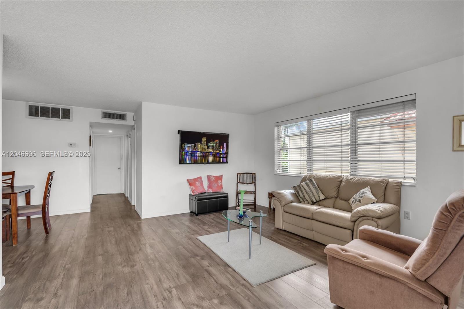 A living room features light wood-look flooring, a beige sofa, and a wall-mounted television — 20327 NE 2nd Ave # 26, Miami FL 33179, MIAMI, FL
