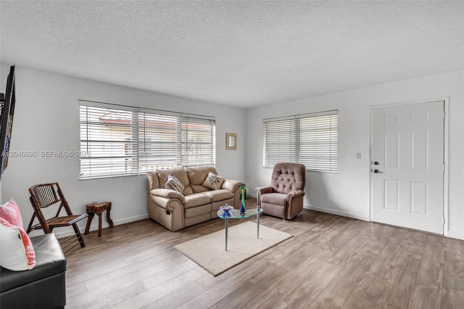 A living room features light wood-look flooring, white walls, a beige sofa, and a recliner — 20327 NE 2nd Ave # 26, Miami FL 33179, MIAMI, FL